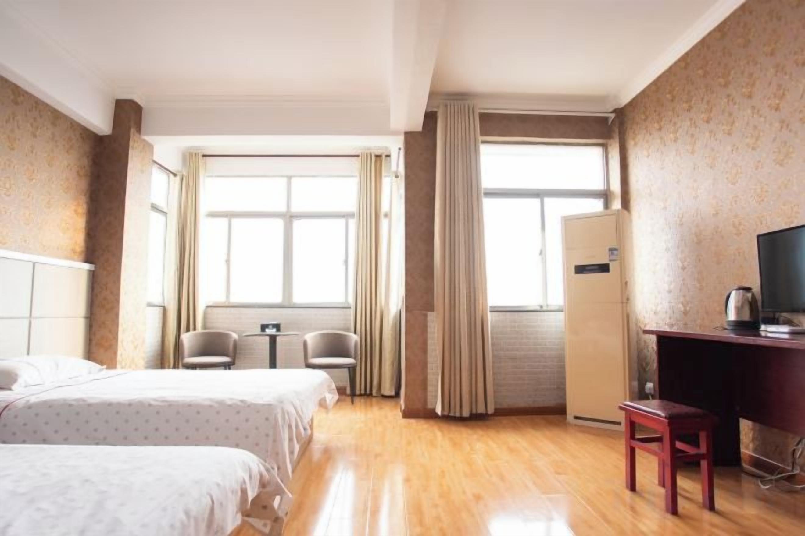 Een hotelkamer met twee bedden, een bureau, een stoel, een televisie en een koelkast.