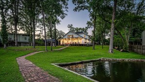 Ein Haus mit einem Ziegelweg, der zu einem Teich führt, umgeben von Bäumen und einem gepflegten Rasen.