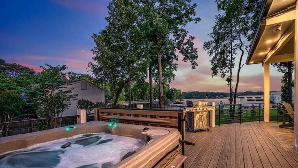 Ein Whirlpool auf einer Holzterrasse mit Blick auf einen See und Bäume im Abenddämmerung.