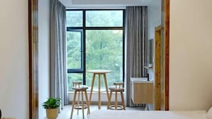 A room with a large window, a bed, a small round table with stools, and a potted plant. - Yunxing Villa (Deqing)