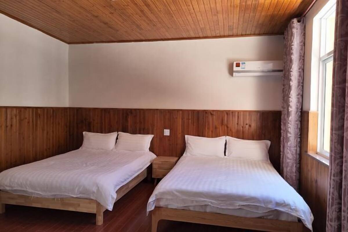Une pièce avec deux lits en bois, un plafond en bois et une fenêtre avec des rideaux.