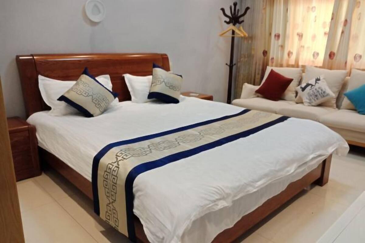 Une chambre à coucher avec un lit en bois, du linge de lit blanc, un canapé et une lampe sur pied.