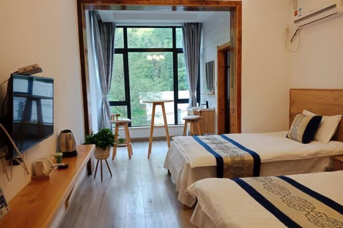 Une chambre d’hôtel avec deux lits, un bureau, une chaise, une télévision et une fenêtre avec des rideaux.