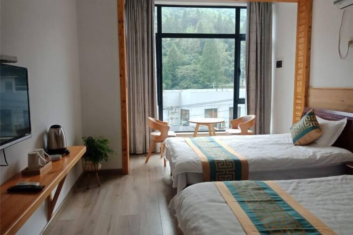 Une chambre d’hôtel avec deux lits, un bureau avec une bouilloire, une télévision et une fenêtre donnant sur des arbres et des immeubles.