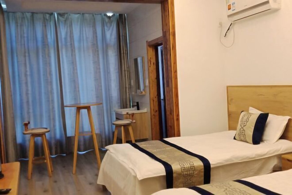 Une chambre d’hôtel avec deux lits, une tête de lit en bois, une petite table, deux tabourets et une fenêtre avec des rideaux.