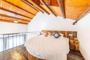 A bedroom with a wooden ceiling, a large bed, a nightstand, and a view of the outdoors. - Yunxing Villa (Deqing)