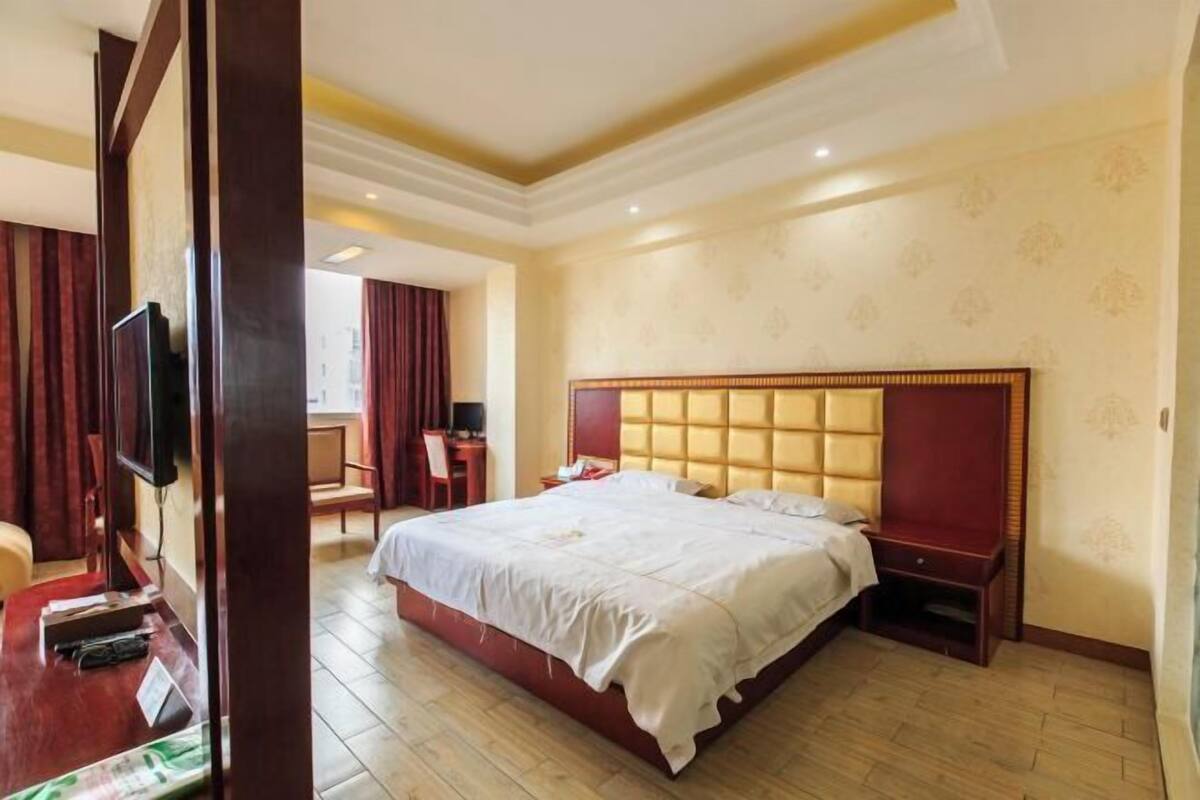 Une chambre d’hôtel avec un grand lit, un bureau avec une chaise, une télévision et une fenêtre avec des rideaux.