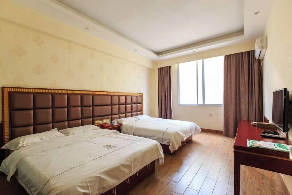 Une chambre d’hôtel avec deux lits, un plancher en bois, une télévision et une fenêtre avec des rideaux.