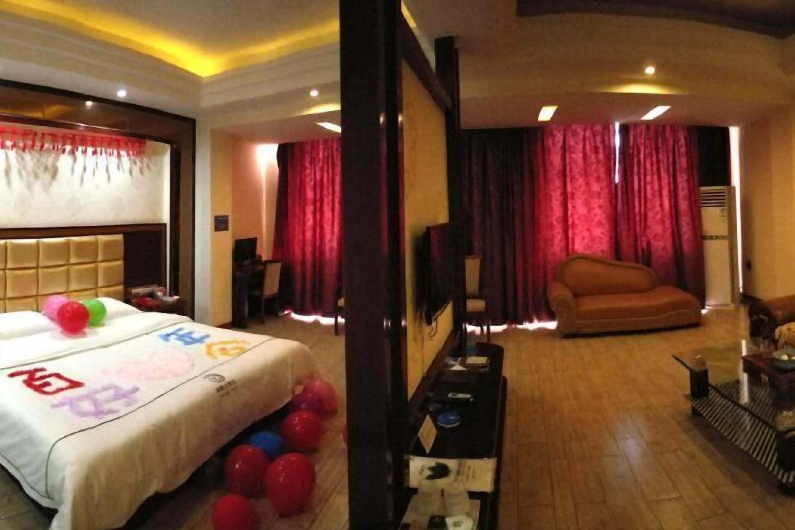 A hotel room with a bed, a sofa, a TV, and a table with a lamp.