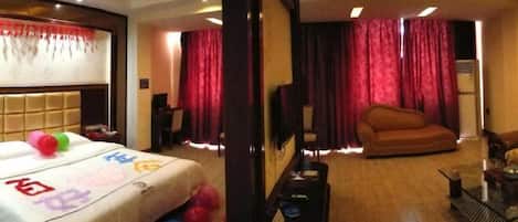 A hotel room with a bed, a sofa, a TV, and a table with a lamp.