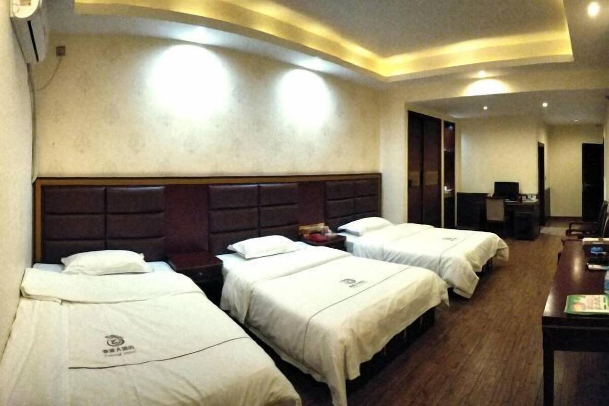 Une chambre d’hôtel avec trois lits, une tête de lit en bois, un bureau avec une chaise et un téléviseur.