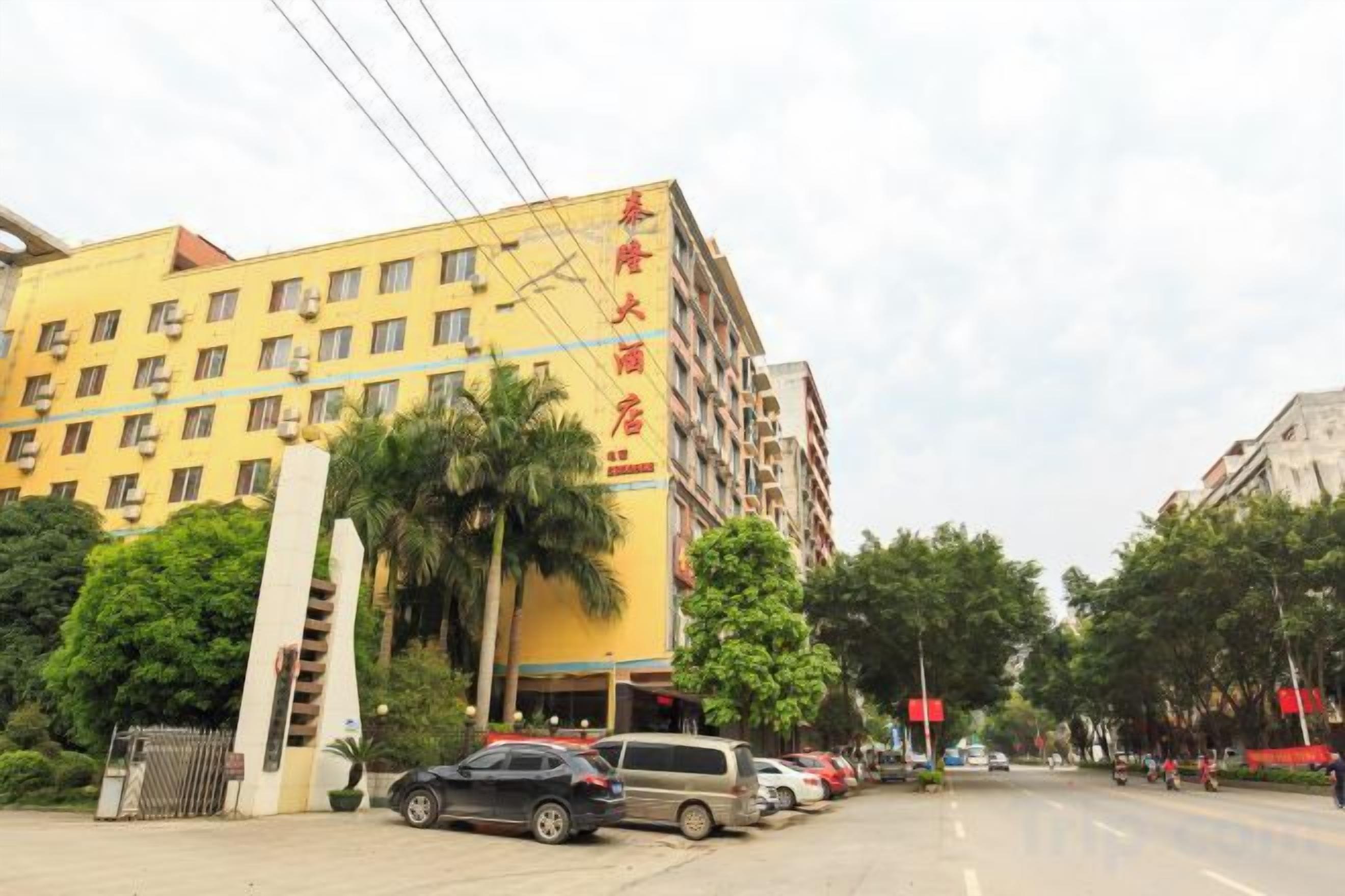 A multi-story hotel with a yellow facade, a gated entrance, and parked cars along the street.