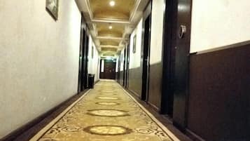 A hotel corridor with a patterned carpet, doors on both sides, and a ceiling with recessed lighting.