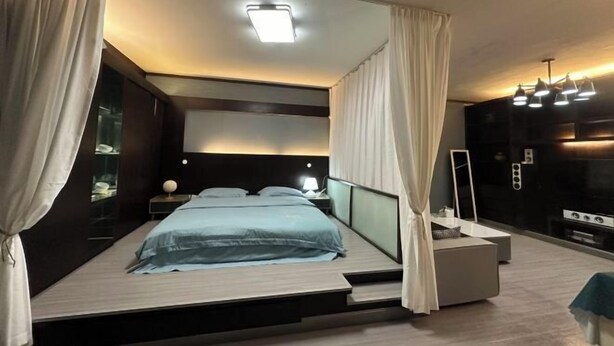 A modern bedroom with a bed, bedside tables, a mirror, and a built-in TV.