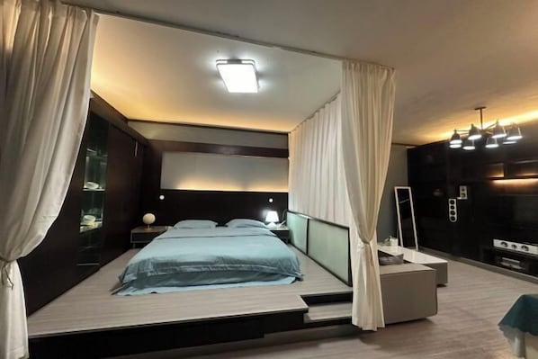 Un dormitorio moderno con cama, mesitas de noche, un espejo y televisión integrada.