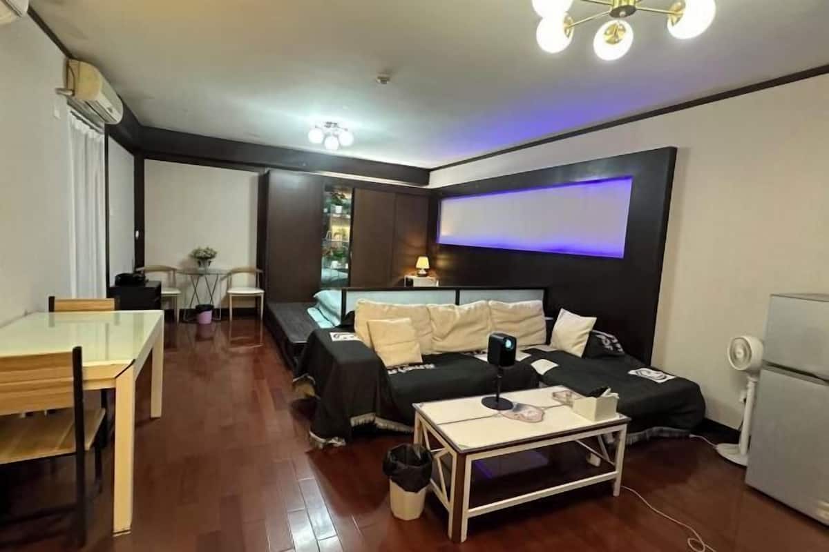 A compact hotel room with a bed, bedside table, desk, chair, and a small kitchenette.