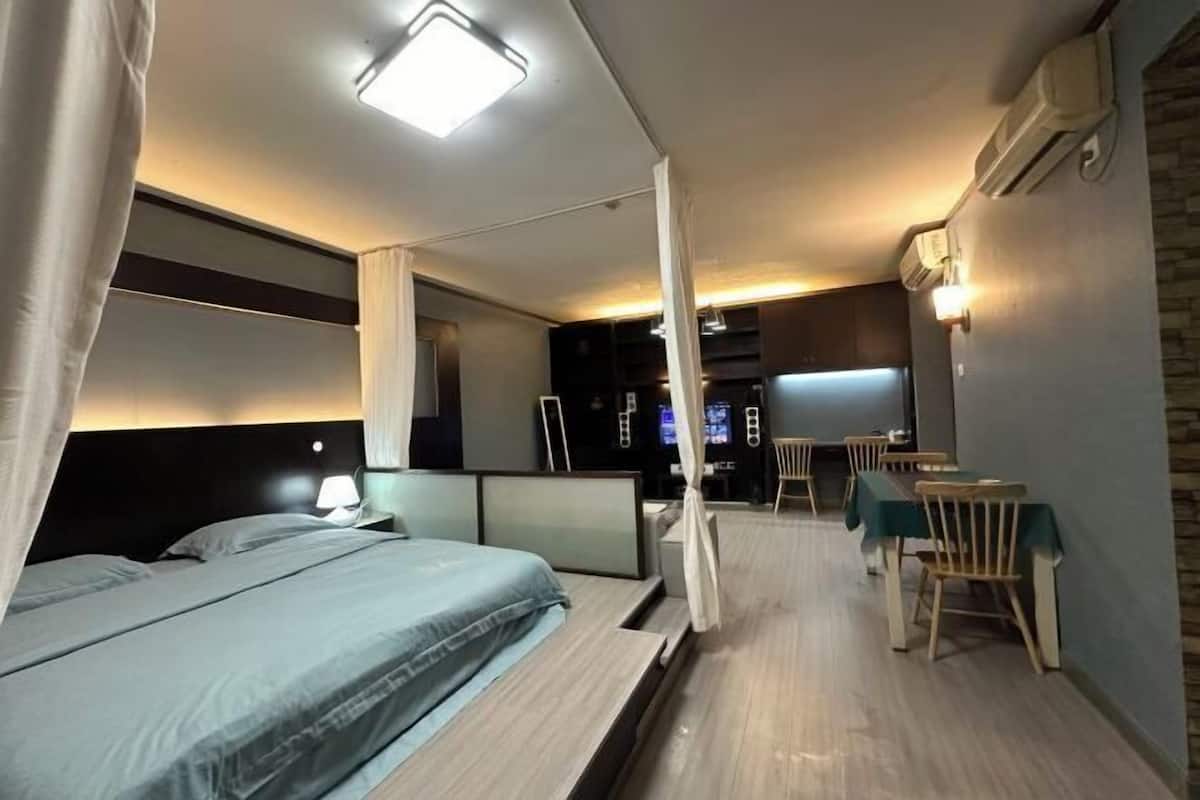 A modern hotel room with a bed, bedside table, and a small dining area with chairs and a table.
