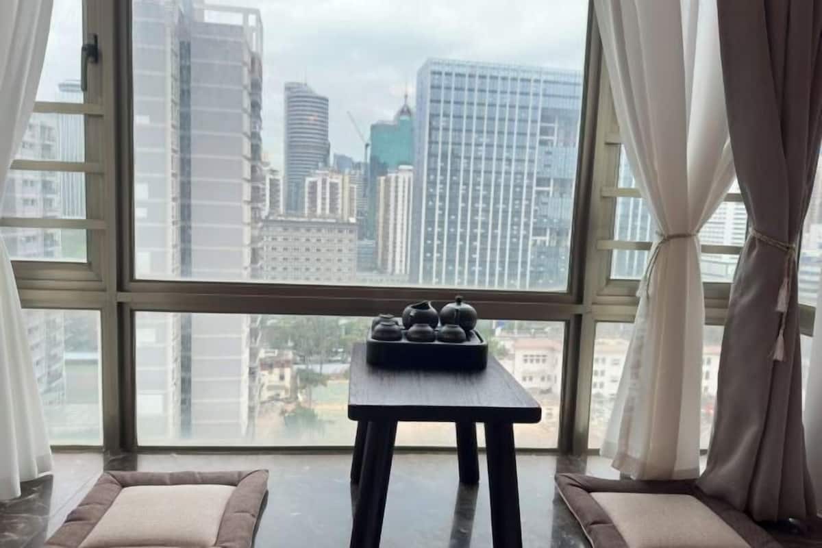 A room with a large window, a small table with teapots, and a cushioned bench.