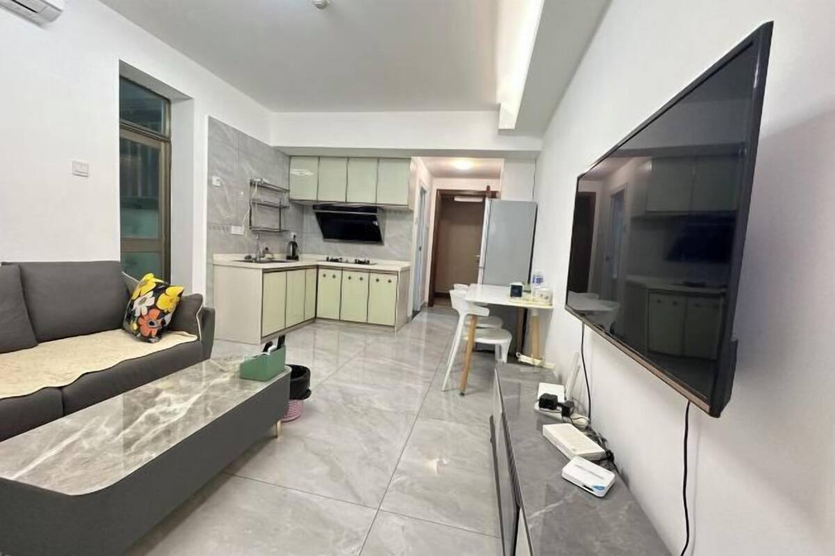 A modern kitchen with a dining area, a sofa, and a TV mounted on the wall.