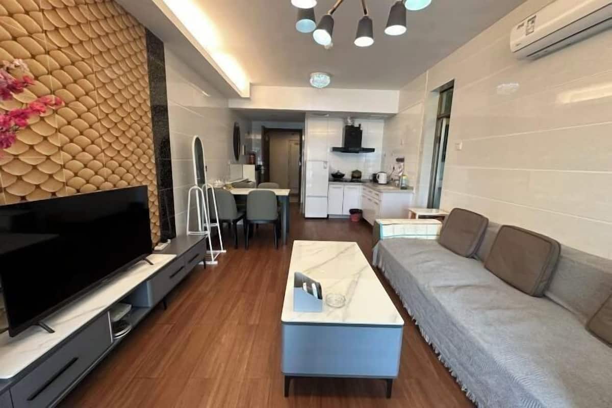 A modern living room with a flat-screen TV, a sofa, a coffee table, and a dining area with chairs.