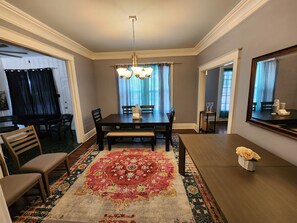Traditional dining room with a dark table and six chairs, surrounded by a large rug and a chandelier.