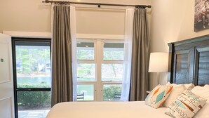 A bedroom with a large bed, a chandelier, a view of the outdoors through a sliding door, and a painting on the wall.