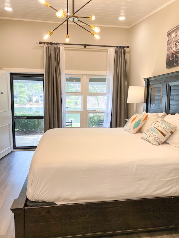 A bedroom with a large bed, a chandelier, a view of the outdoors through a sliding door, and a painting on the wall.