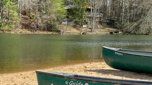 Two green boats on a sandy shore with a lake and trees in the background.