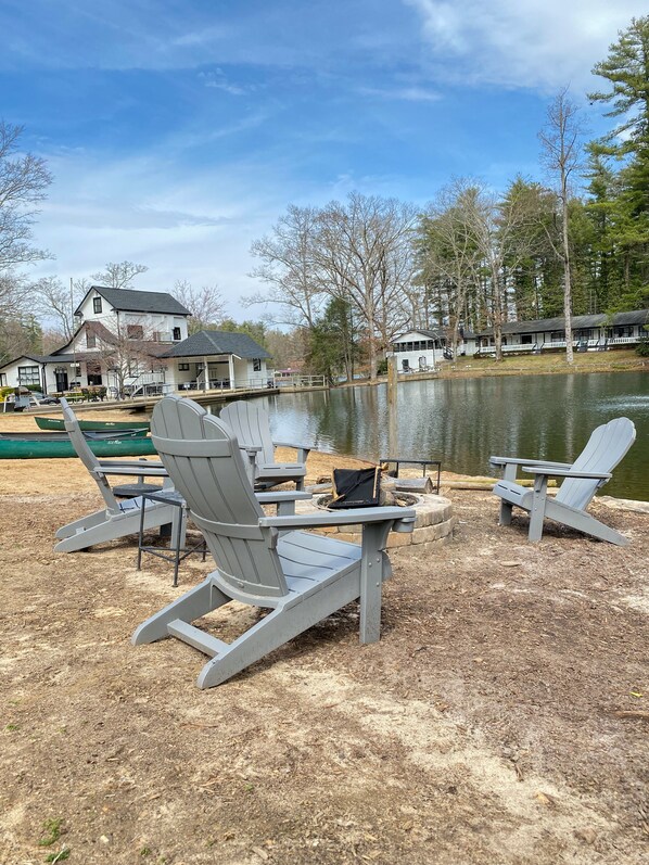 Un entorno frente al lago con sillas Adirondack, un muelle y una casa con porche con vista al agua.