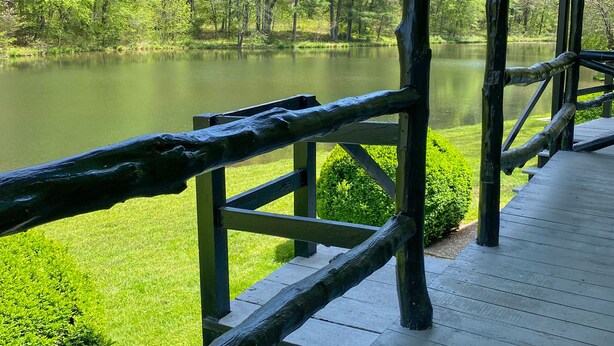 A wooden deck overlooking a calm lake with lush greenery and trees in the background.