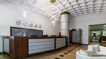 Uma área de recepção com design moderno, incluindo um balcão de atendimento, uma parede com relógios exibindo diferentes fusos horários e um teto com padrão geométrico.