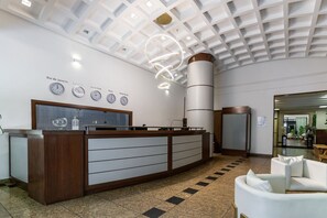 A reception desk with a modern design, a ceiling with a geometric pattern, and clocks displaying time in various cities. - (902-B) Studio com Vista Mar e Comodidades (Rio de Janeiro)