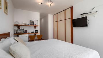 Um quarto com cama, escrivaninha com cadeira, televisão e guarda-roupa.