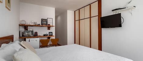 Un dormitorio con una cama, un escritorio con una silla, un televisor y un armario.