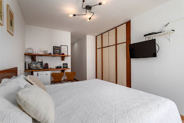 Un dormitorio con una cama, un escritorio con una silla, un televisor y un armario.
