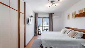 Quarto de hotel com cama, escrivaninha, cadeira, janela com cortinas e luminária no teto.