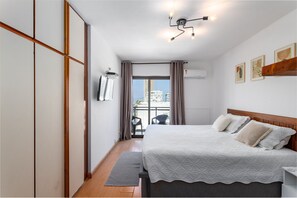 A hotel room with a bed, a desk, a chair, a window with curtains, and a ceiling light fixture. - (902-B) Studio com Vista Mar e Comodidades (Rio de Janeiro)