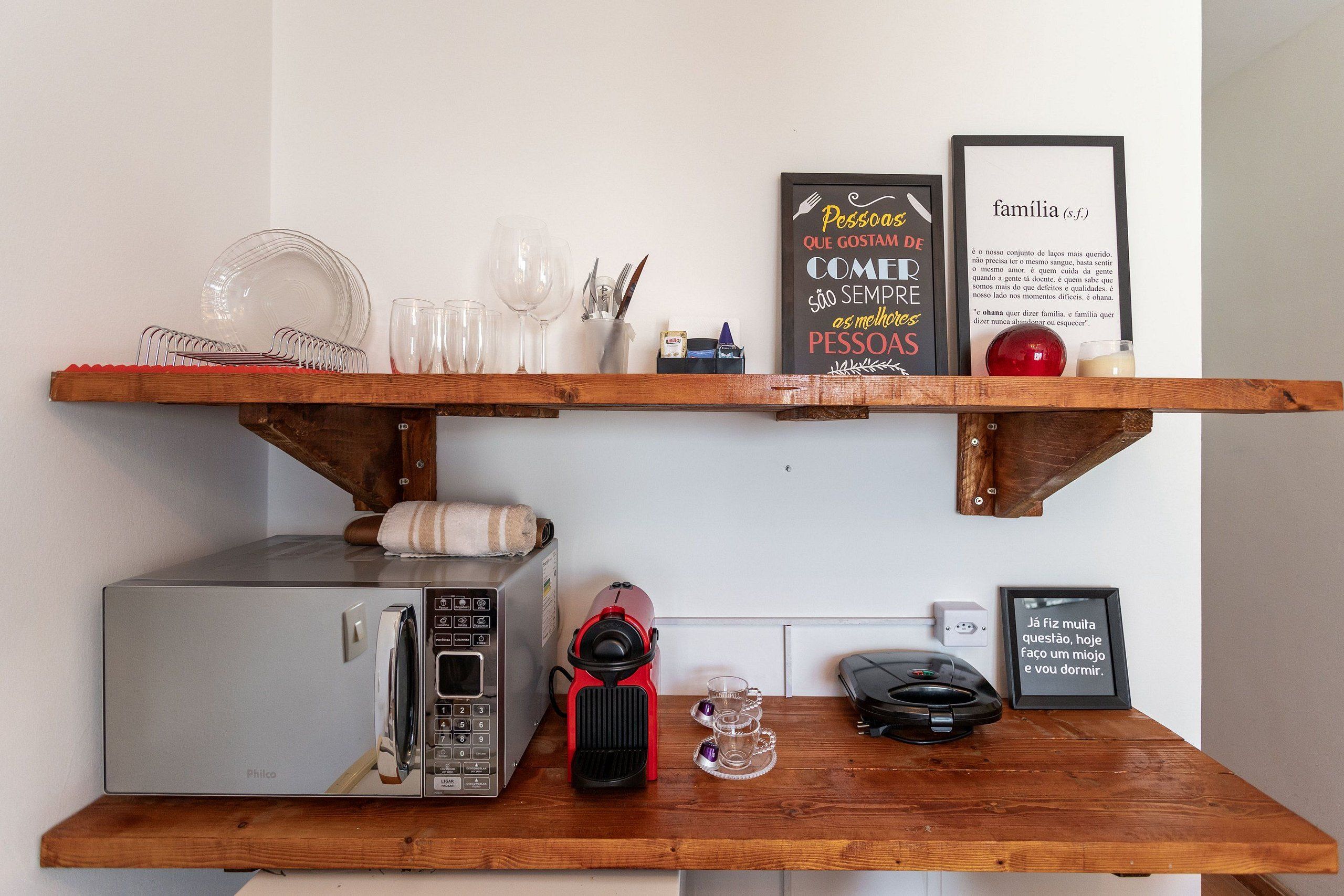 Cozinha compacta com micro-ondas, torradeira e cafeteira em bancada de madeira.