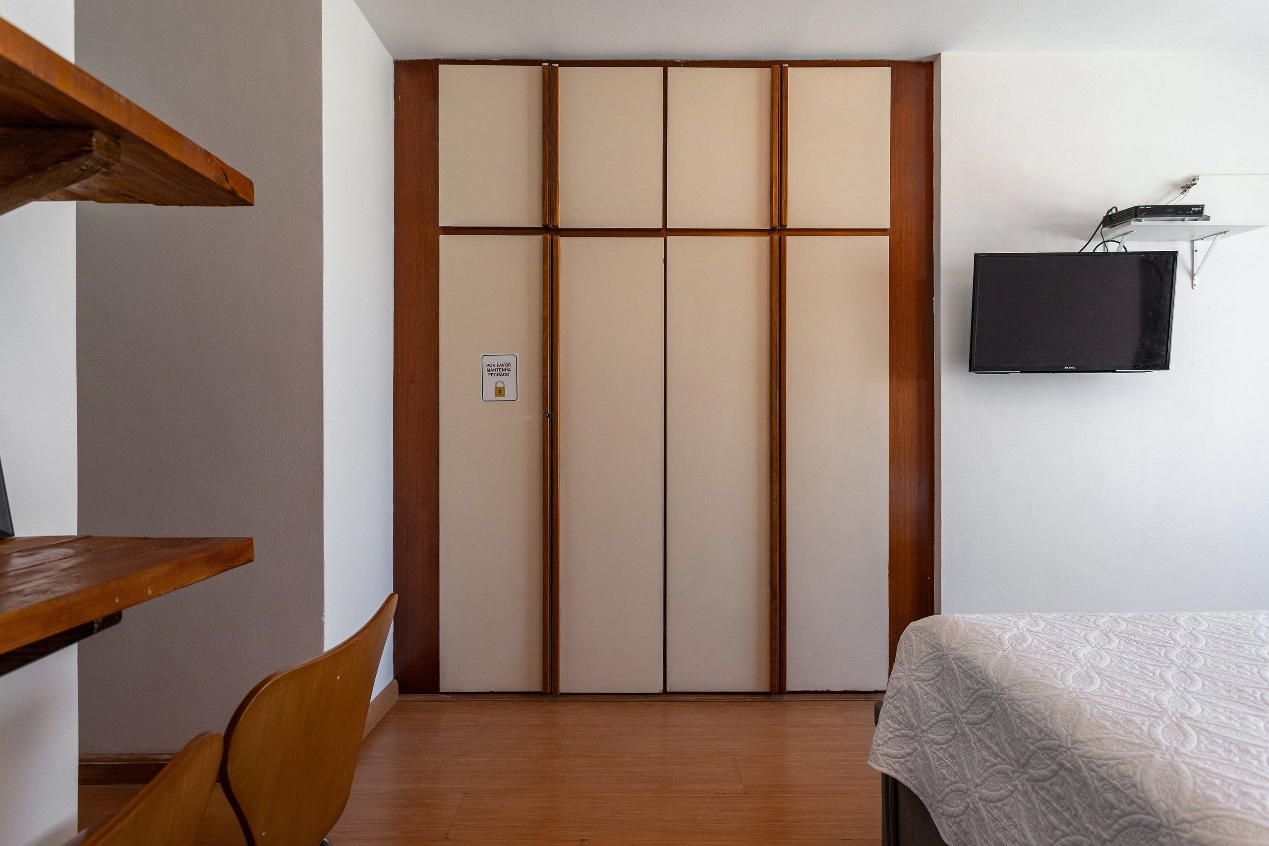 Una habitación con armario, cama, escritorio y televisor.