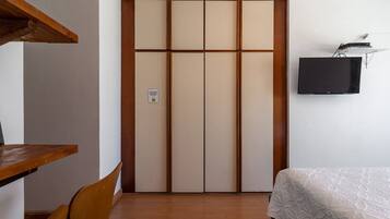 Quarto com guarda-roupa, cama, escrivaninha e televisão.
