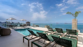 Área de piscina no terraço, com espreguiçadeiras e guarda-sóis, com vista para o horizonte da cidade e o mar.