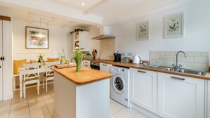 A modern kitchen with white cabinetry, a wooden island, a built-in washing machine, and a dining area with a table and chairs.
