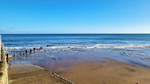 A beach with a clear sky, calm sea, and a concrete barrier.