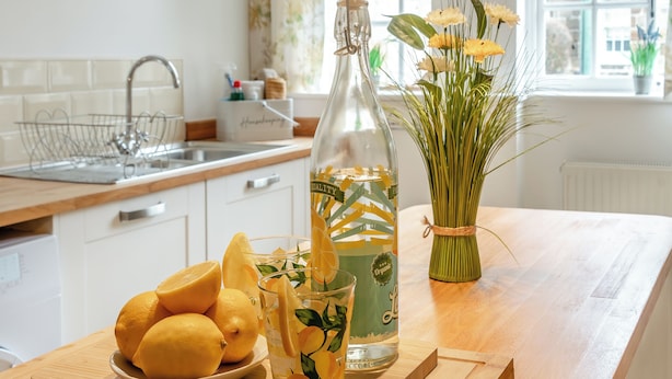 A kitchen counter with a bottle, a glass, and a plate of lemons.