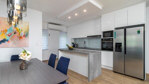 A modern kitchen with a central island, stainless steel appliances, and a dining area with a table and chairs. - 2 bedroom stunning apartment in Pobri (Pobri)
