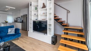 A modern living space with a blue sofa, white shelving unit, and a wooden staircase. - 2 bedroom stunning apartment in Pobri (Pobri)
