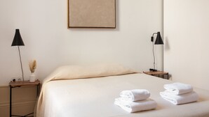 A neatly made bed with white linens and folded towels, two bedside tables with lamps, and a framed artwork on the wall. - VIVA  Alameda Suites 3 (Porto)