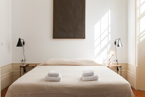 Hotellihuone, jossa on suuri sänky, kaksi yöpöytää valaisimineen ja taulu seinällä.