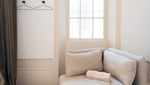 Una habitación con un sofá color beige, una ventana con persianas y dos perchas en la pared.