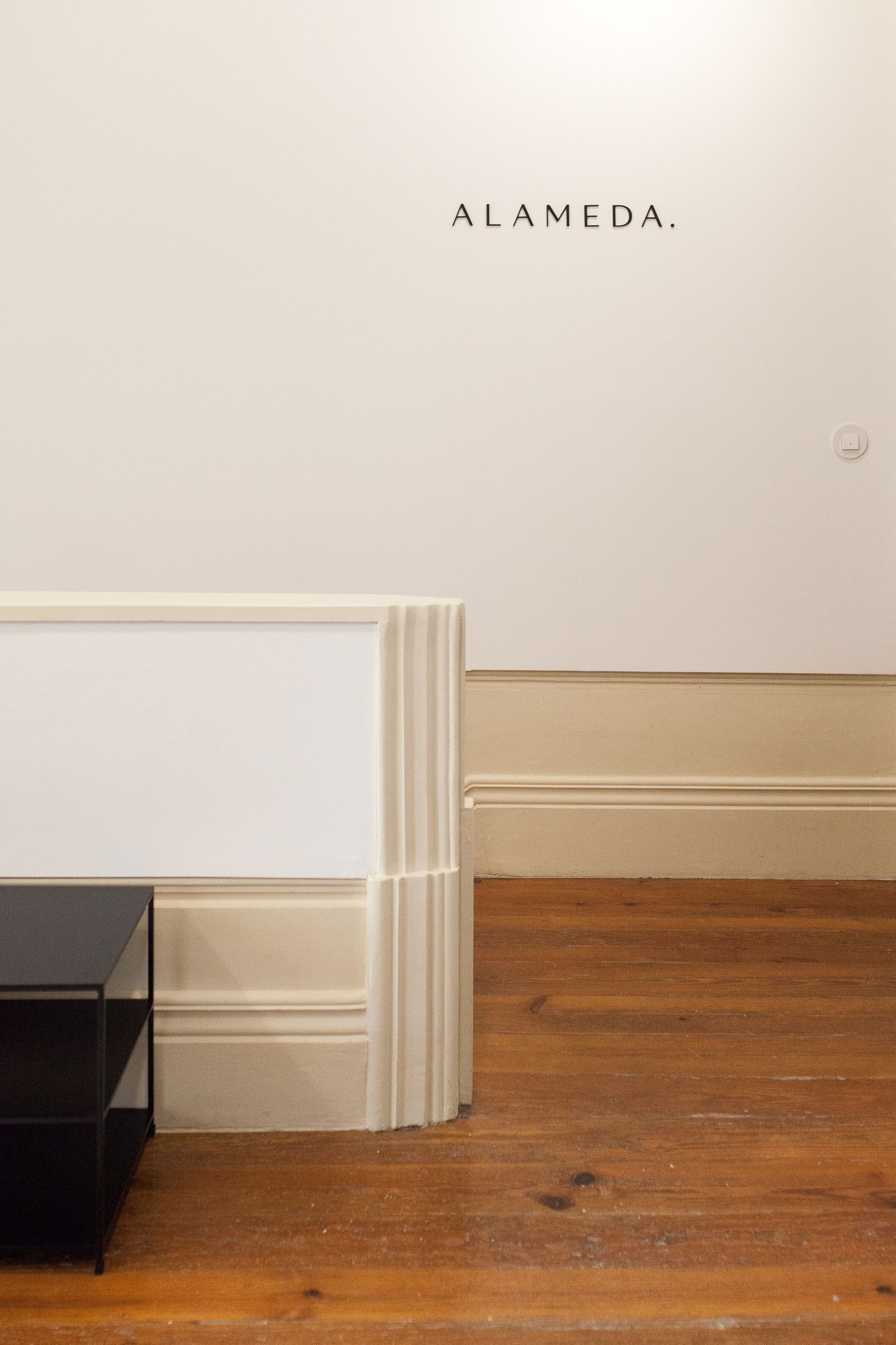 A room with a wooden floor, a white wall, and a black table.